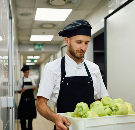 Male cook carrying fresh vegetables from the pantry.